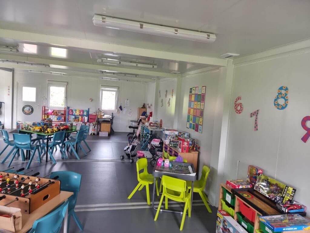 Colorful children's playroom with multiple tables, chairs, and a variety of toys and educational materials