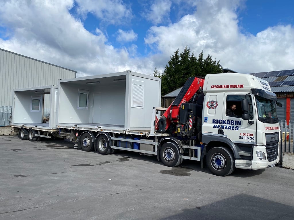 Truck hauling modular portable buildings to a construction site, with 'Rickabin Rentals' on the vehicle