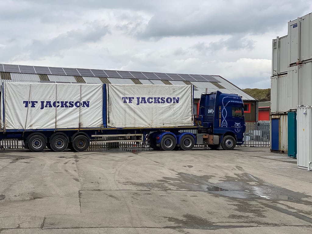 DAF truck loaded with TF Jackson-branded covered modular units at an industrial yard
