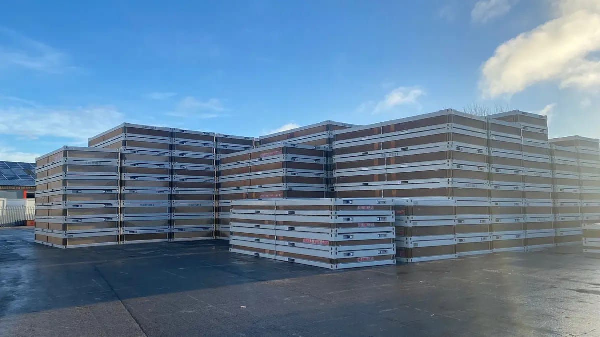Large stacks of flat-pack modular building sections in a storage yard
