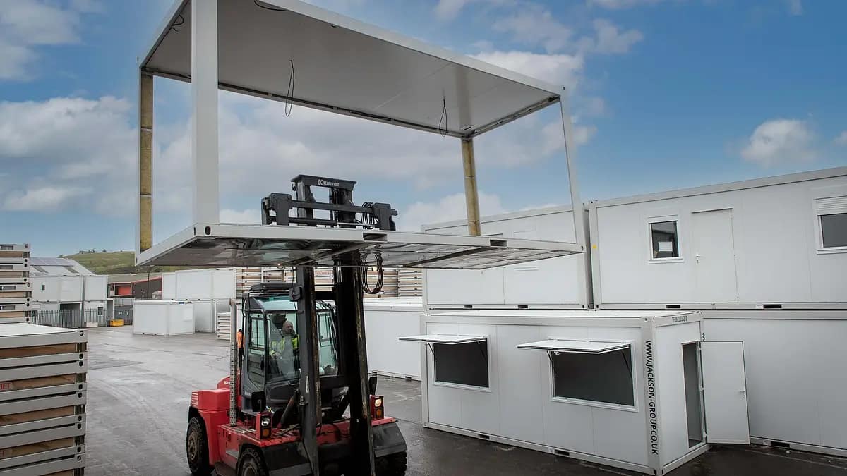 A forklift lifting a large modular building component in an industrial yard