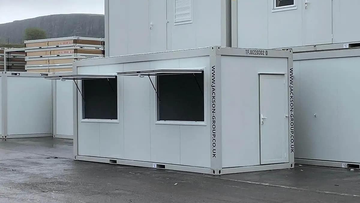 "Modular building with TF Jackson branding and website details, featuring a service window, against a backdrop of stacked units