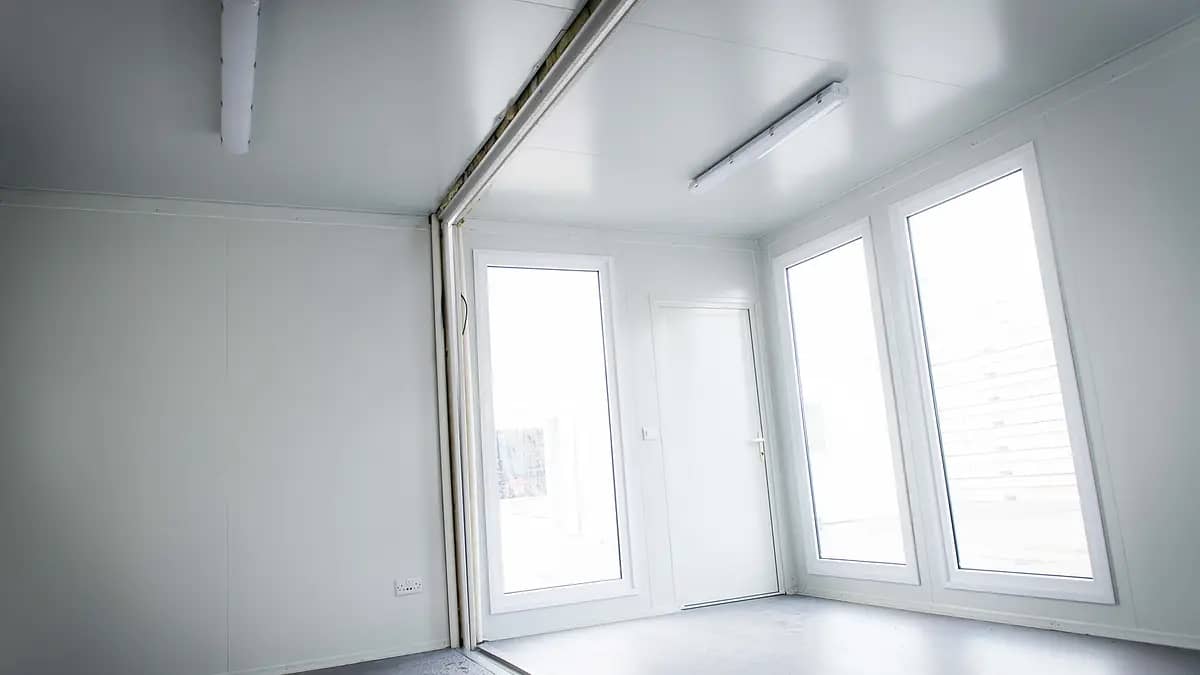 Interior of a bright modular room with white walls and large windows allowing natural light to fill the space.