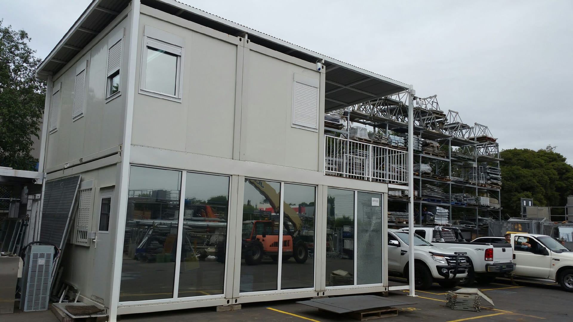 Two-story modular office building with large windows and surrounded by industrial equipment and vehicles