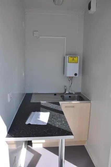 Compact kitchenette inside a modular unit with a sink and electrical water heater