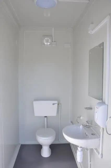 Small bathroom setup within a modular unit featuring a toilet and washbasin