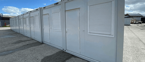 Row of portable sleeping units with white shutters in an outdoor setting, under a clear sky