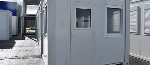 Close-up view of a portable building entrance with a window and shutters, located in a storage yard