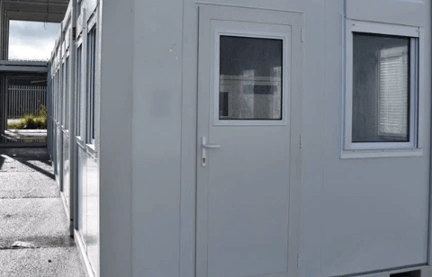 Close-up view of a portable building entrance with a window and shutters, located in a storage yard