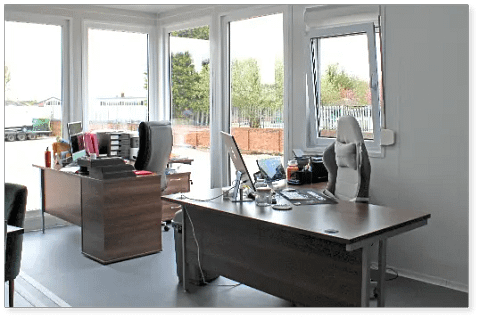 Office space with two desks, chairs, and computers, bright interior.