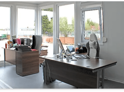 Office space with two desks, chairs, and computers, bright interior.