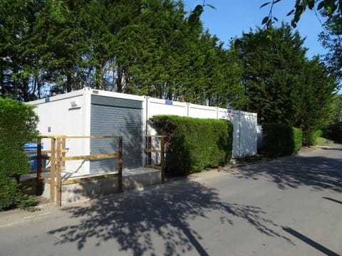 White modular building nestled between lush greenery, near a paved road