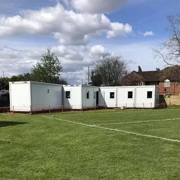 White modular classrooms arranged in a row on a green field with a cloudy sky overhead.