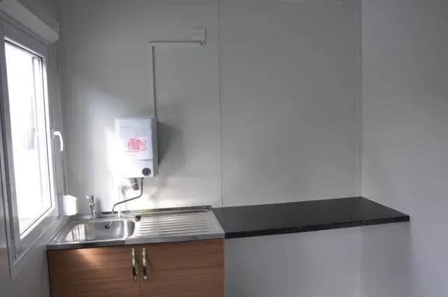 Small kitchenette setup inside a modular building, featuring a wooden cabinet and sink