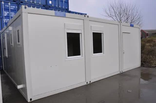 Exterior view of a long white modular building with several windows, set on a wet pavement