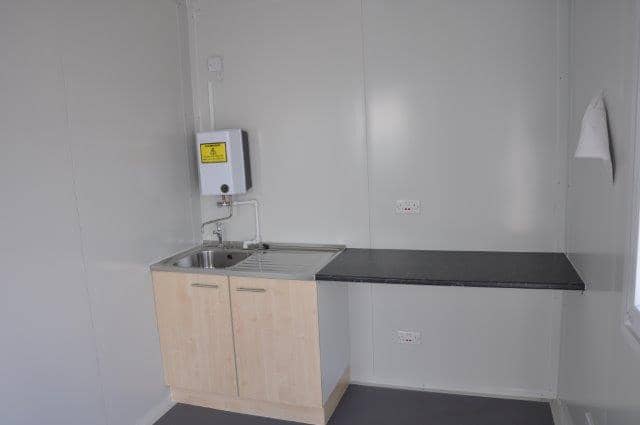 Compact kitchenette inside a modular unit featuring a wooden cabinet, sink, and electrical water heater