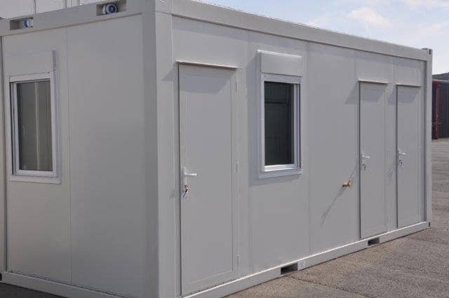 Exterior of a white modular building with two doors and windows, placed on a paved area