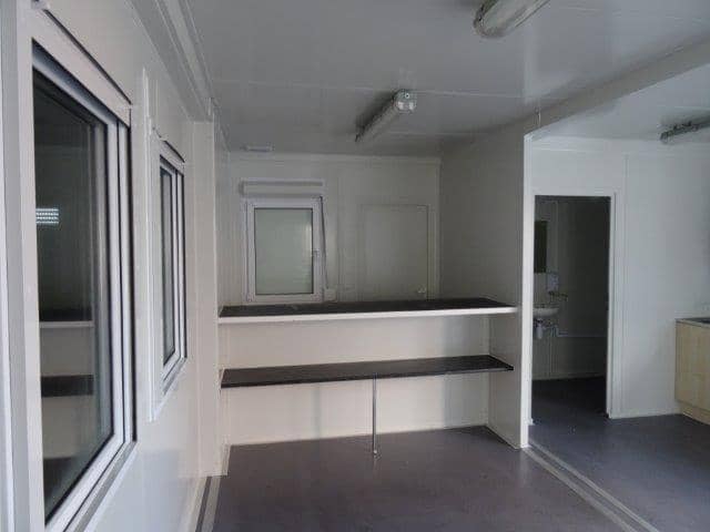 Interior of a modular building featuring a counter and windows, with a separate room visible in the background