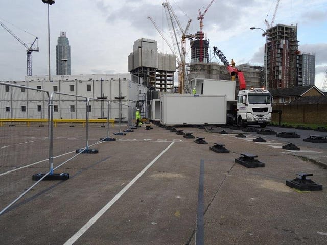 Modular building being installed at a construction site with urban skyline and cranes in the background