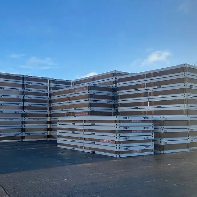 Large stacks of flat-pack modular building sections in a storage yard