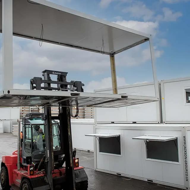 A forklift lifting a large modular building component in an industrial yard