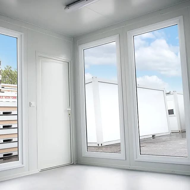 Bright, empty interior room with large windows overlooking stacked container units outside.