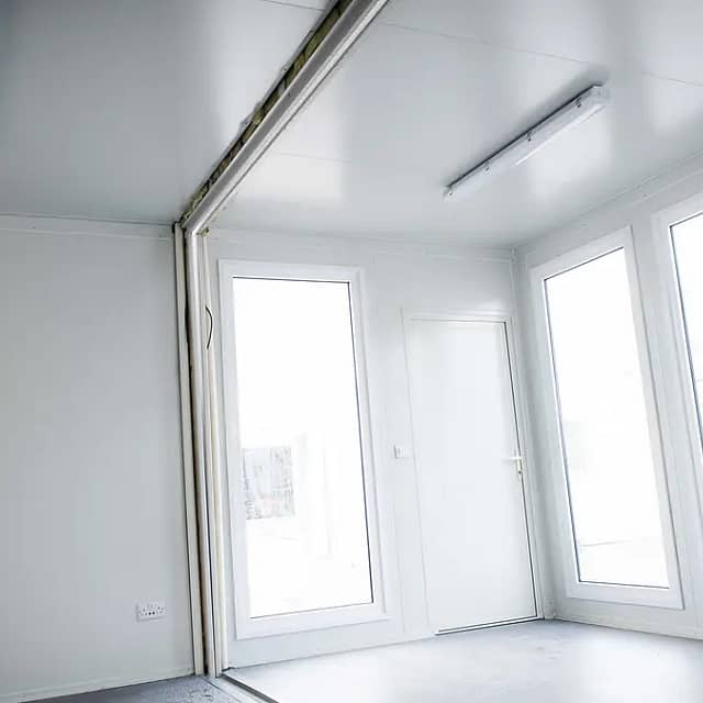 Interior of a bright modular room with white walls and large windows allowing natural light to fill the space.