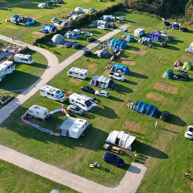 Aerial view of a campsite with tents, caravans, and vehicles on a sunny day