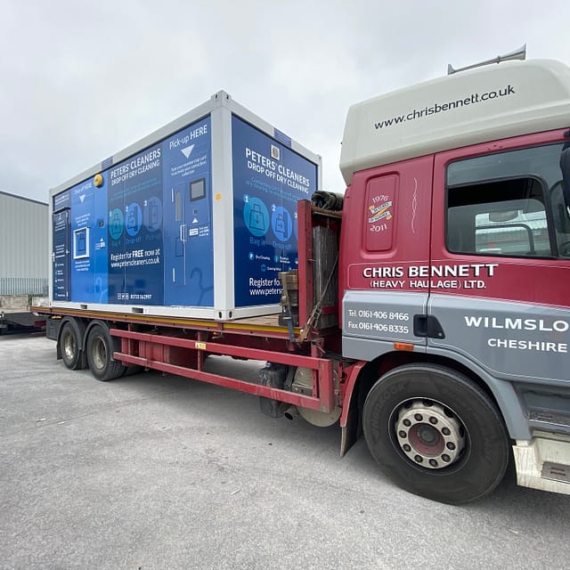 A red Chris Bennett heavy haulage truck with advertising for Peter's Cleaners on its side, parked in an industrial area