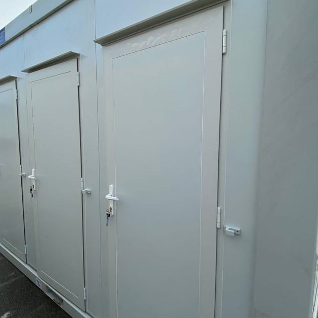 Portable toilets lined up outdoors on a wet ground, indicating temporary outdoor facilities
