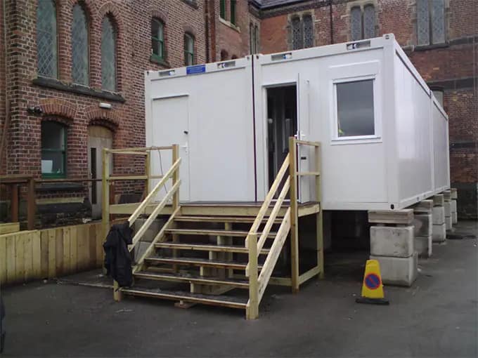 Modular building with a wooden staircase set against a backdrop of a brick building