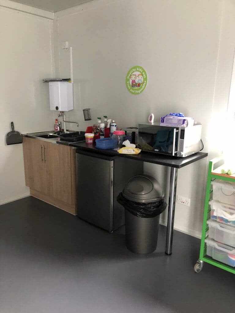 Interior of a small kitchenette with a sink, storage cabinets, and various cleaning supplies.