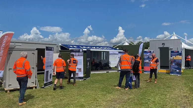 People in safety vests at a T.F. Jackson portable building exhibit on a sunny day.
