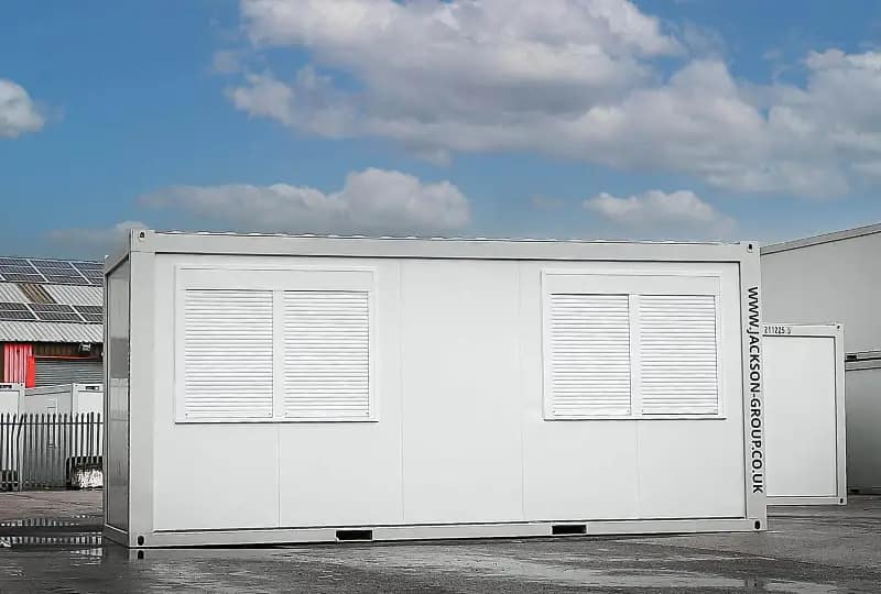 White portable container unit with closed window shutters, placed outdoors with 'WWW.JACKSON-GROUP.CO.UK' branding on the side