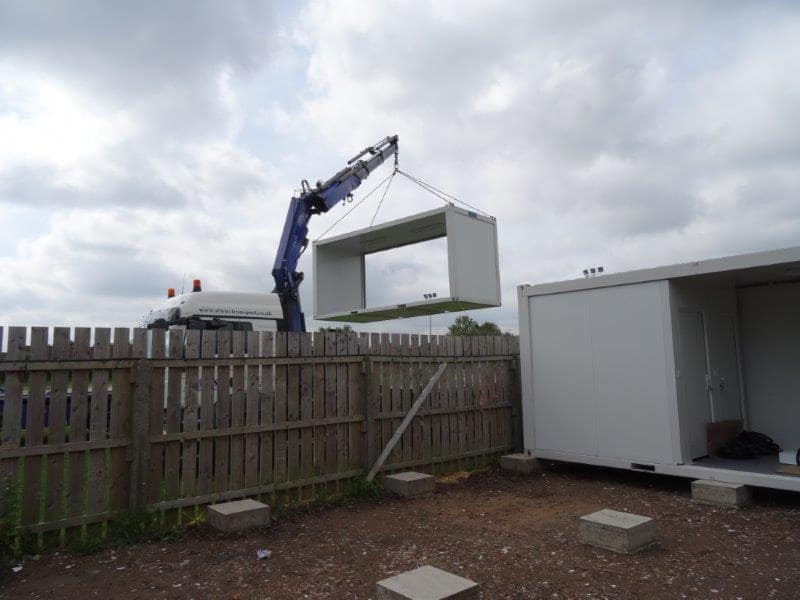 Crane lifting a modular building onto a foundation at a residential site.