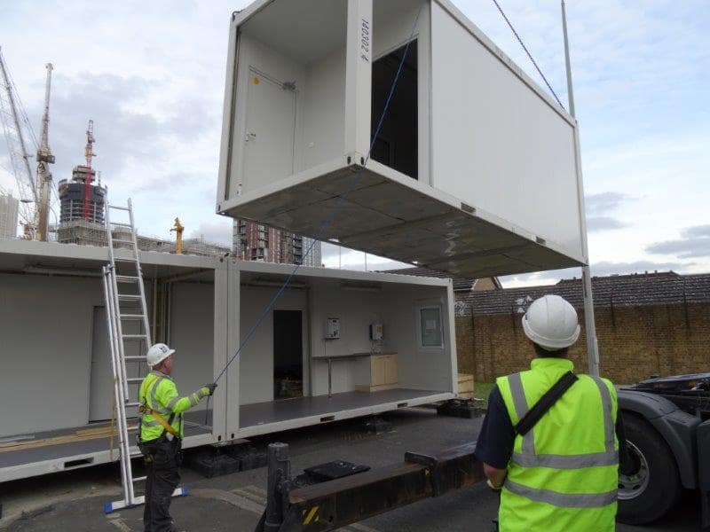 Construction workers guiding a modular unit as it is being craned onto a trailer at an urban site