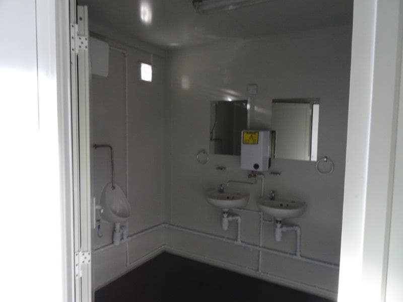 Interior of a modular bathroom featuring urinals, washbasins, and mirrors