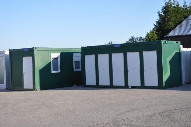 Green modular buildings with white doors set in a paved lot.
