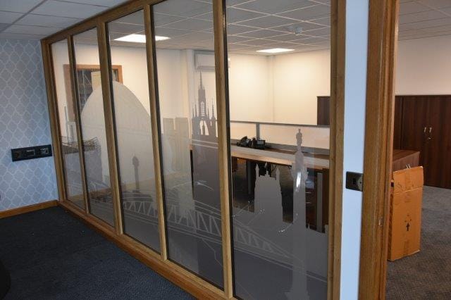 View through a wooden-framed glass partition into an office space with desks and computers