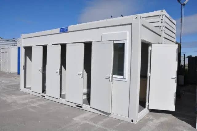 White modular building with multiple doors open, showcasing interior bathrooms