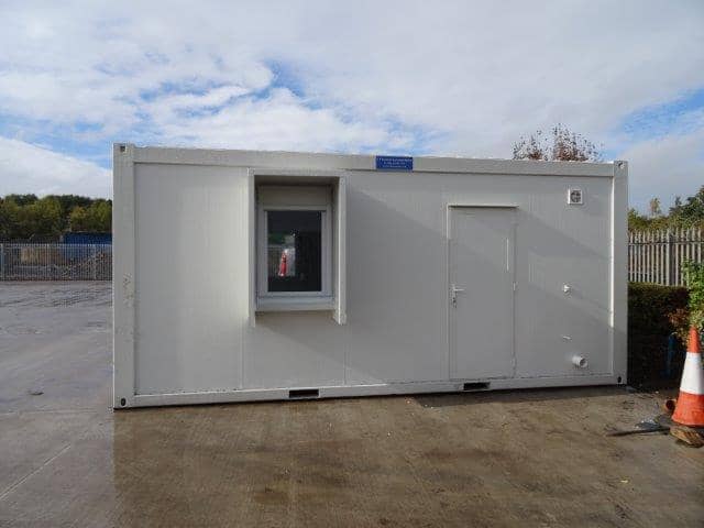 Side view of a white modular building with a single door and window, on a wet concrete surface